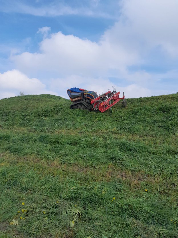 Radiografische rupsmaaier op steile helling met bewolkte hemel